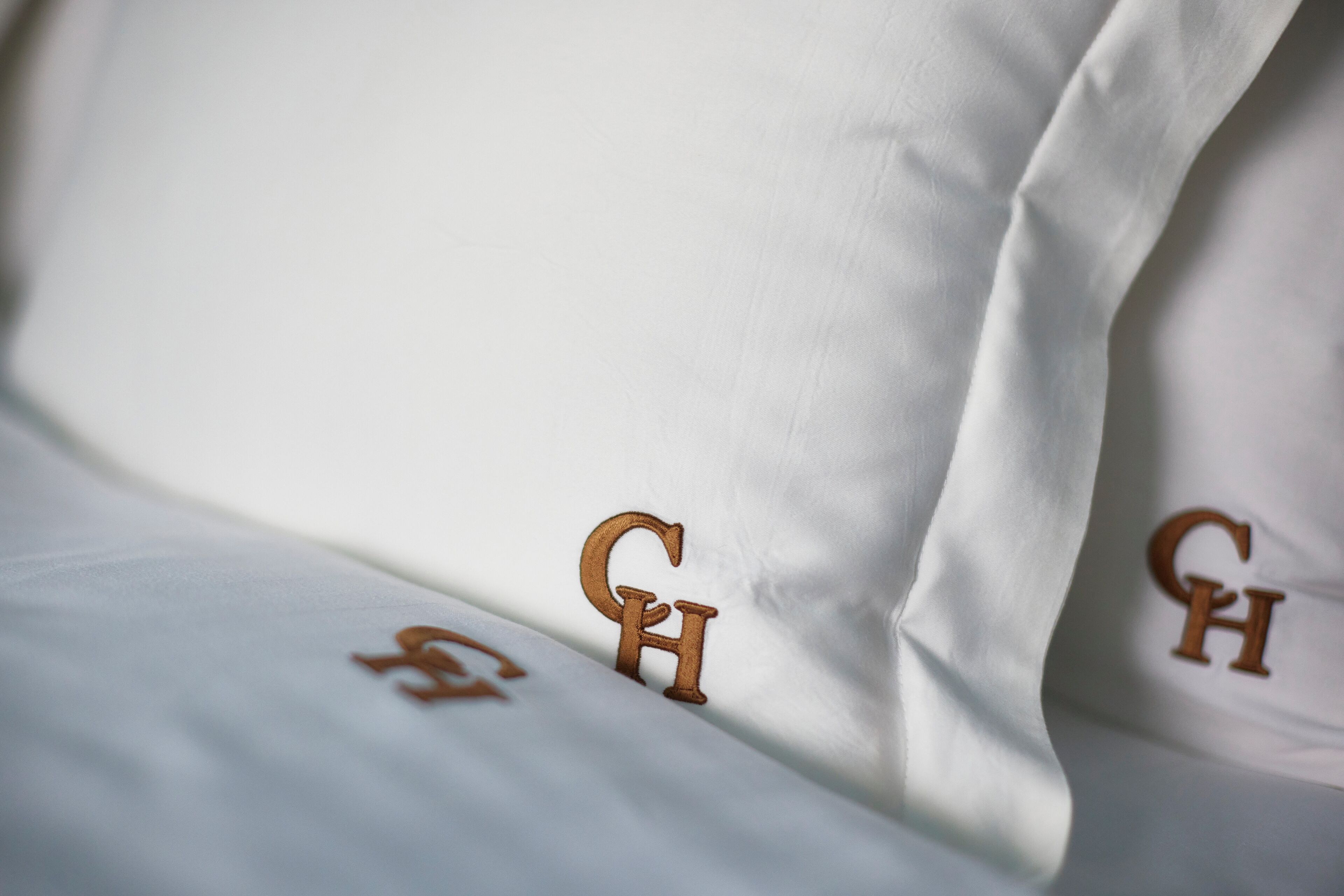 Ein Detailbild eines Bettes mit aufgestickten Buchstaben 'GH' auf Kissen und Bettdecke.
