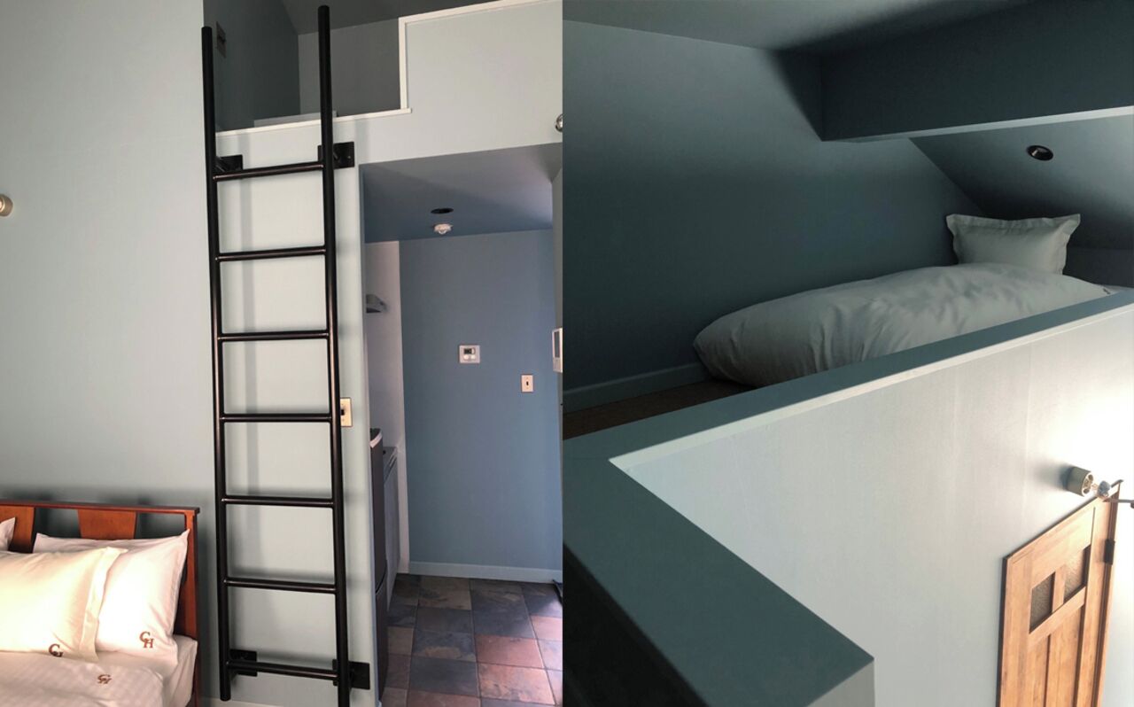 A room with a bed, a ladder, a door, and a staircase.