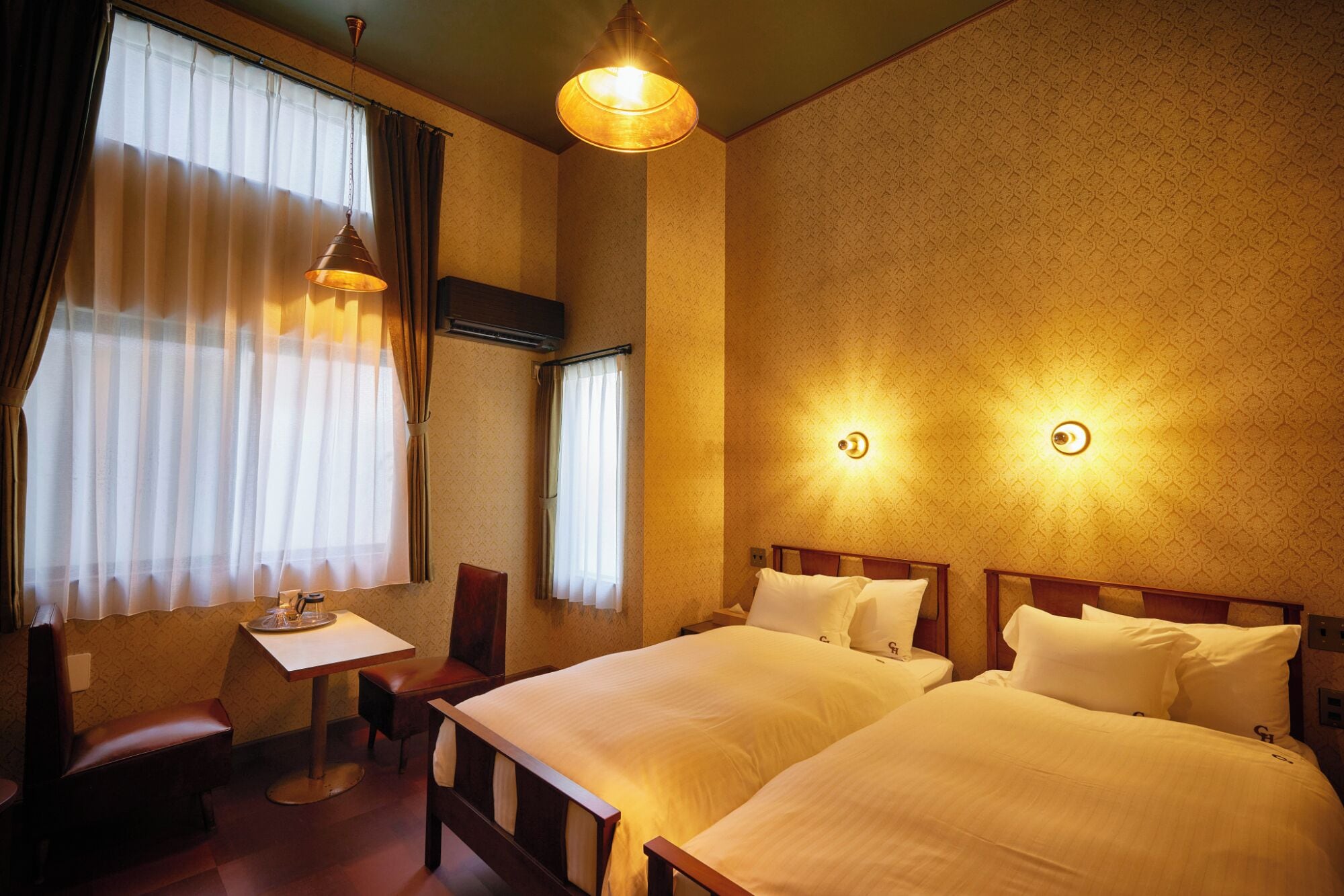 A hotel room with two beds, a desk, a chair, and a window with curtains.