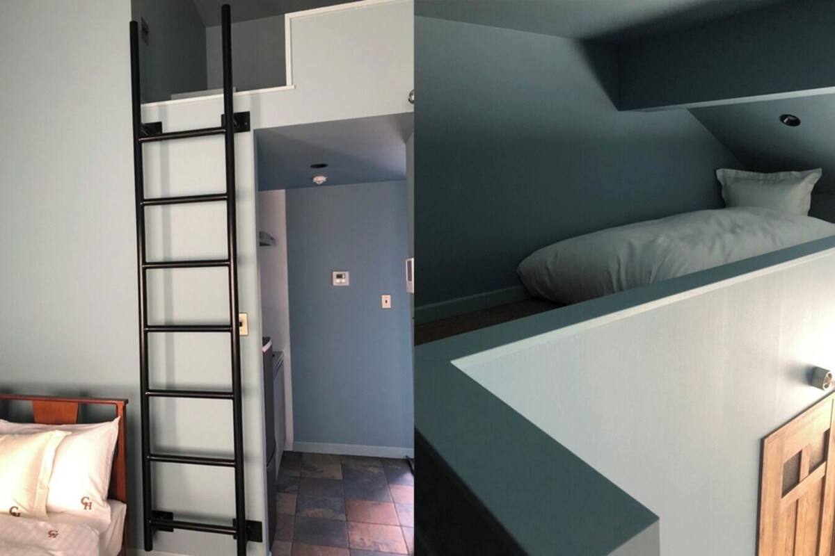 A room with a bunk bed, a ladder, a door, and a small window.