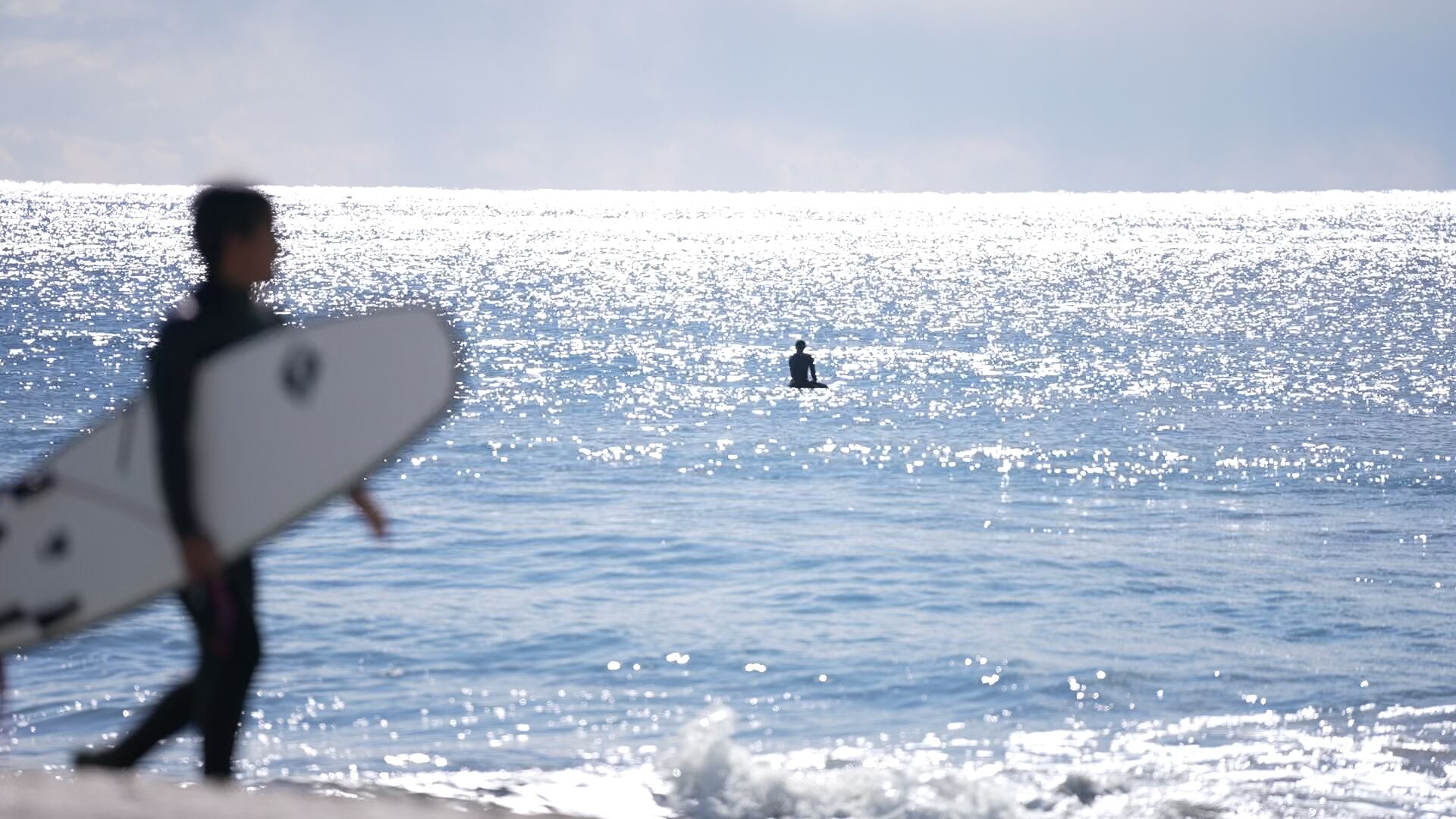 A person carrying a surfboard walking towards the ocean.