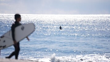 Una persona lleva una tabla de surf caminando hacia el océano.