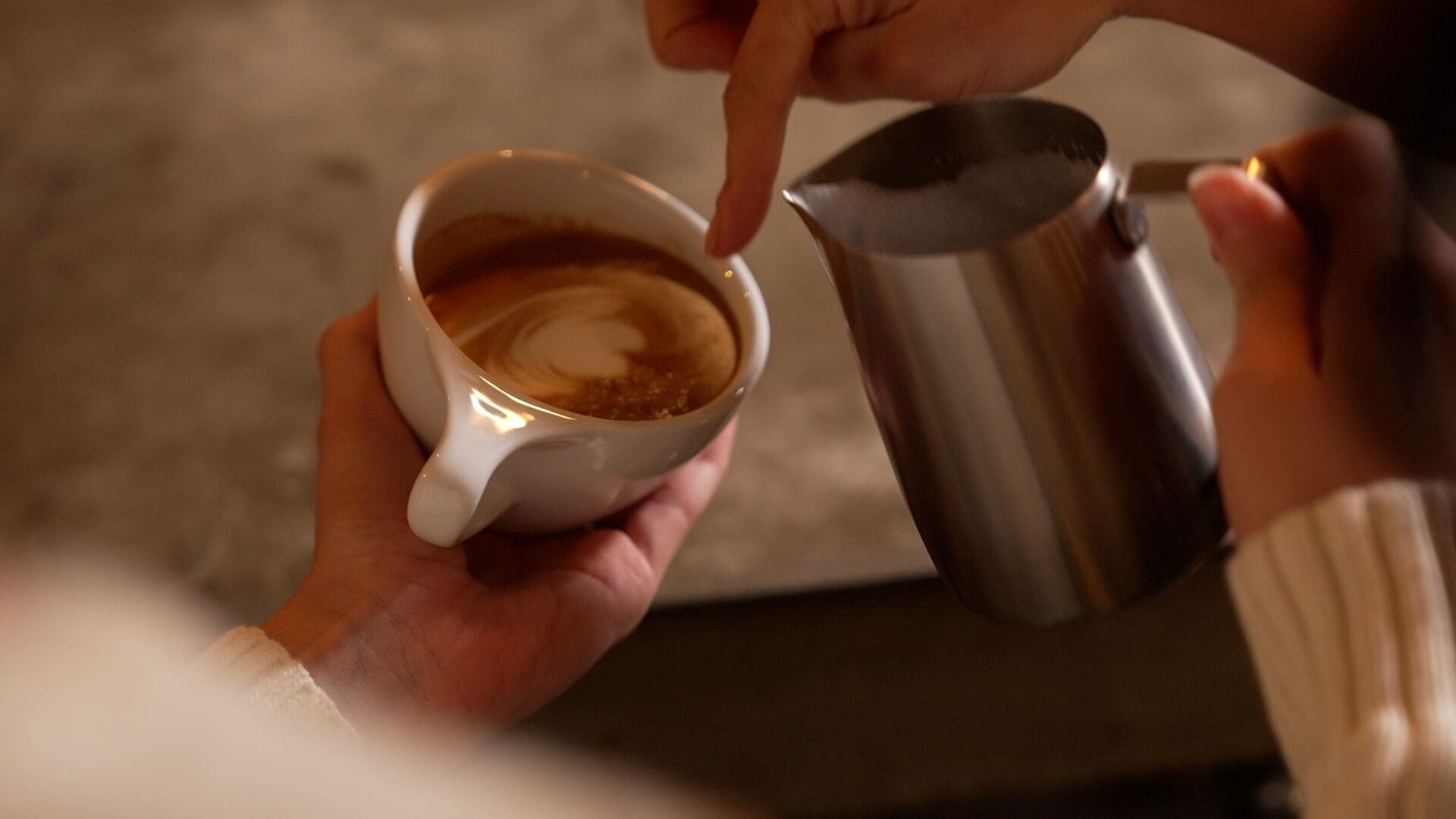 En person som håller i en kaffekopp och en metallkanna.