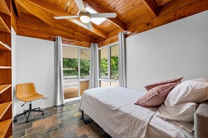 Relax in this spacious room with a large bed, central ceiling fan, and a comfortable chair.