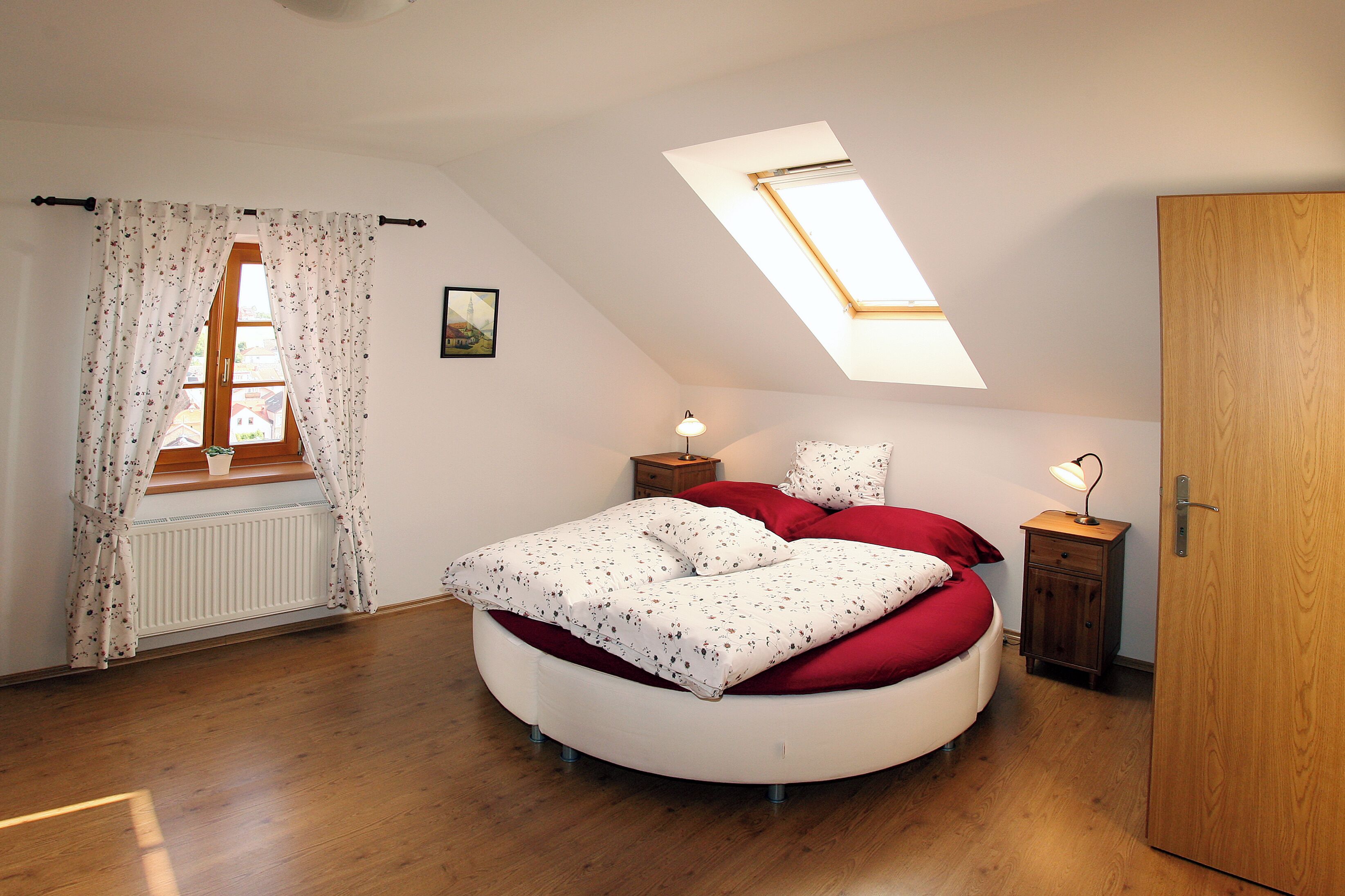 Un dormitorio con tragaluces, una cama redonda, un radiador y suelo de madera.