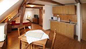 A cozy attic bedroom with a wooden bed, a small desk, and a kitchenette. - Penzion u Chodského Hradu (Domazlice)