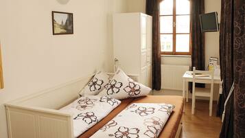 Ein Schlafzimmer mit Bett, Schreibtisch, Kleiderschrank, einem Fenster mit Vorhängen und einem Wandbild.