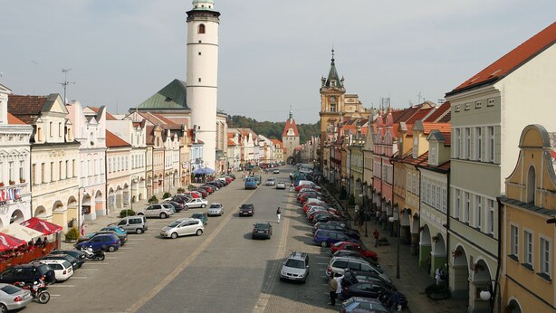 A street lined with parked cars and historic buildings with a prominent tower. - Penzion u Chodského Hradu (Domazlice)