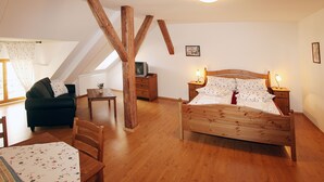 A bedroom with a wooden bed, a green sofa, a wooden dining table, and a small side table. - Penzion u Chodského Hradu (Domazlice)