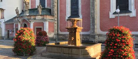 A courtyard with a fountain, two statues, and a building with arched windows.