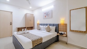 A neatly arranged hotel room with a large bed, bedside tables, a wardrobe, a ceiling fan, and a wall-mounted mirror.