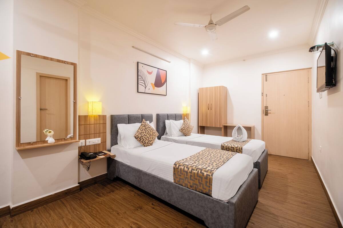 A hotel room with two beds, a ceiling fan, a mirror, a wall-mounted TV, and a wooden wardrobe.