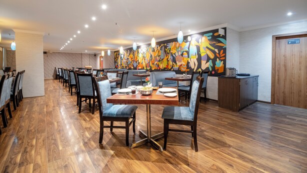 A spacious dining area with wooden flooring, modern chairs, and a vibrant abstract mural on the wall.