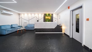 A modern reception area with a black floor, white walls, and a reception desk. There are two blue sofas and a small table with a plant.