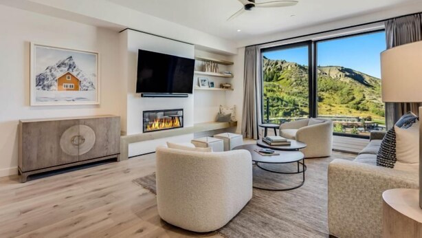 A modern living room with a fireplace, comfortable seating, a flat-screen TV, and a scenic mountain view.