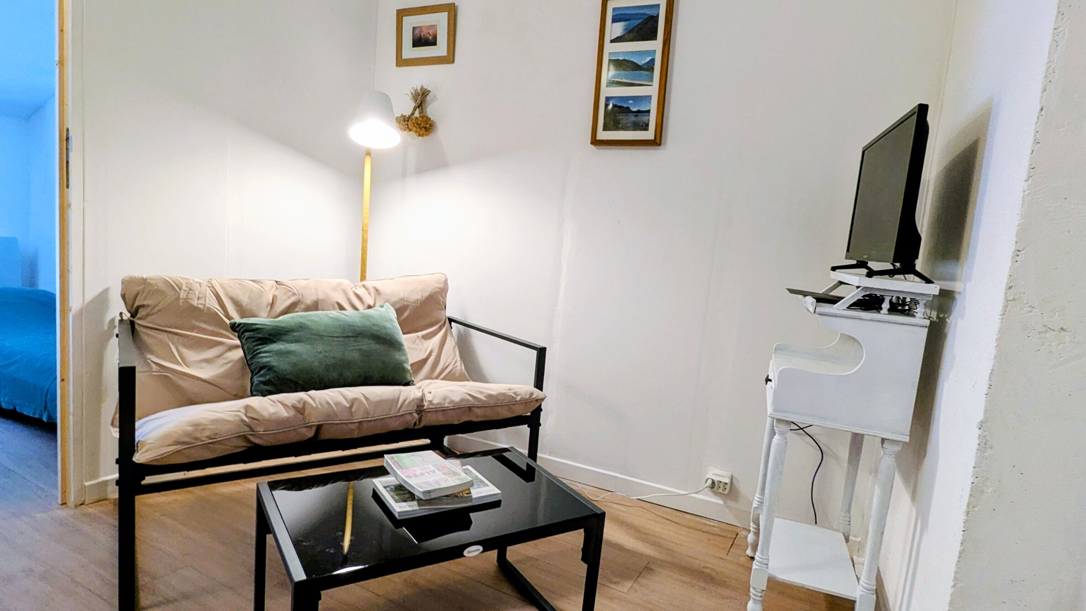 Uma sala de estar com um sofá, uma mesa de centro com livros, um abajur e um rack de TV com um monitor.