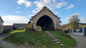 A stone structure with an arched entrance, surrounded by a grassy area and a pathway leading to it. - Vacation rental lakes, vineyards and mountains area (MASSIGNIEU DE RIVES)