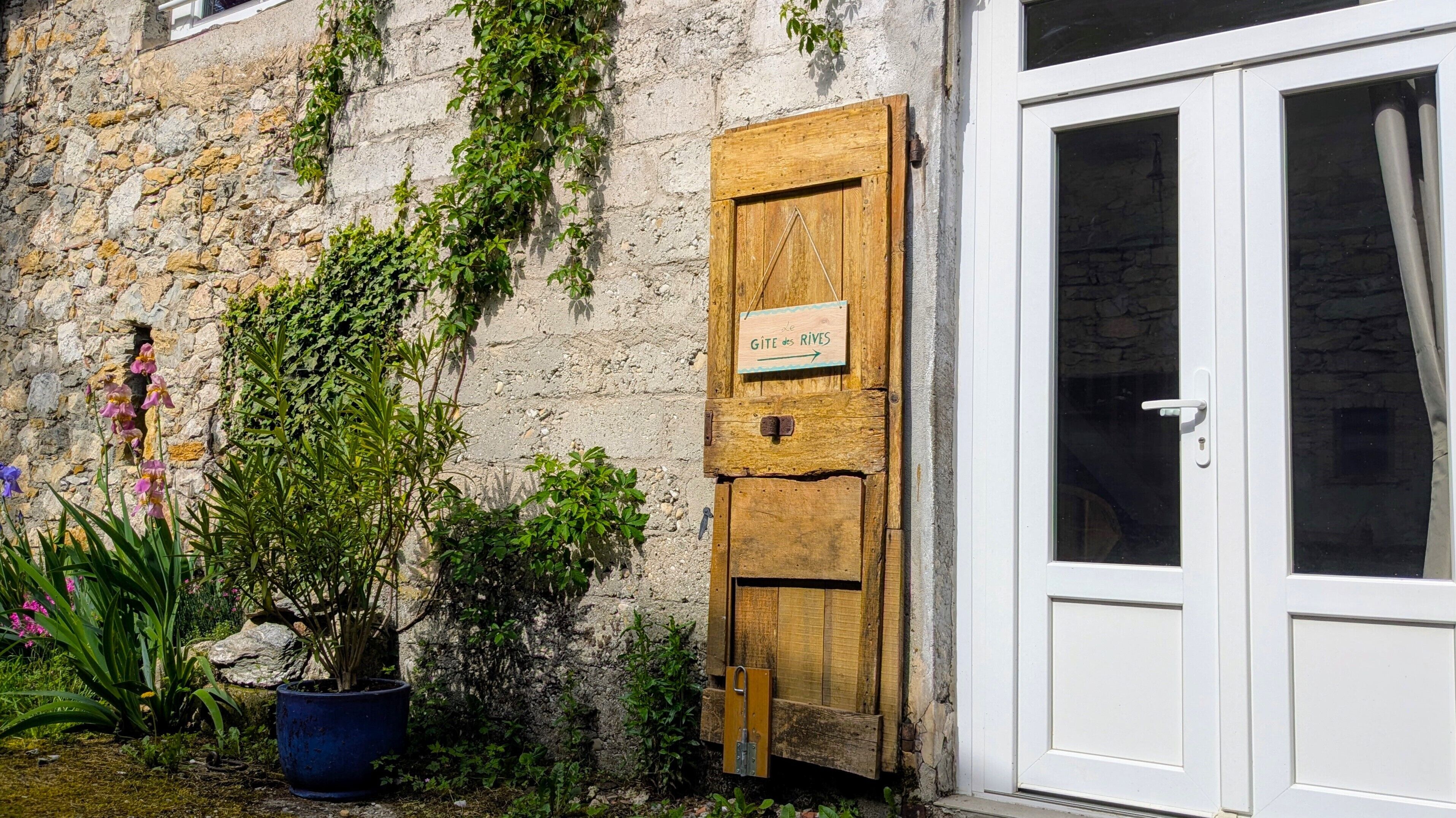 Un edificio rústico de piedra con una puerta de madera que dice “GITE des RIVES” y una puerta blanca.