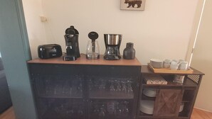 A kitchen area with a coffee maker, blender, and kettle on a wooden countertop. There are plates and cups on a shelf below. - Holiday home in Zuienkerke with a terrace (Zuienkerke)