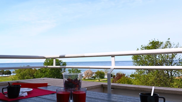 Een balkon met een tafel gedekt voor twee, met uitzicht op een prachtig zeegezicht en groen.