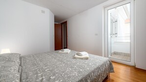 Een slaapkamer met twee bedden, een schuifdeur naar een balkon en een houten vloer.