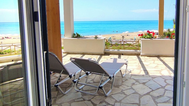 Une porte vitrée donnant sur une terrasse extérieure avec vue sur l’océan, deux fauteuils et une structure en forme de pergola.
