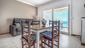 Un comedor con mesa y sillas, un sofá, y vista al océano a través de un ventanal.