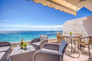 A terrace with wicker furniture, a table with a bottle and glasses, and a view of the sea. - ALMADRAVA BEACH 2 Roses (Rosas / Roses)