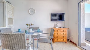 A compact living space with a dining area, a television mounted on the wall, and a wooden dresser. - ALMADRAVA BEACH 2 Roses (Rosas / Roses)