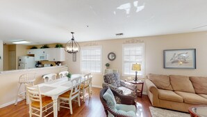 A spacious living room with a beige sofa, a dining area with a white table and chairs, and a kitchen in the background. - Golf Course Oasis Inviting 3BRVilla Pawleys Island (Pawleys Island)