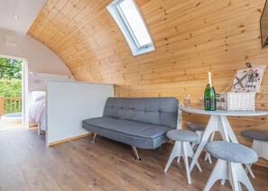 Une pièce chaleureuse avec un canapé gris, une petite table ronde sur laquelle se trouvent une bouteille et des verres, et un panier en osier.