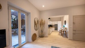 A modern living room with a TV, a dining area with a table and chairs, a kitchen with cabinets and a sink, and a sliding glass door leading to an outdoor area. - Sublime 2 Pièces Avec Jardin (Villefranche-sur-Mer)