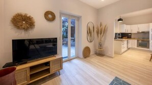 A modern living room with a flat-screen TV, a wooden entertainment unit, and a sliding glass door leading to a patio. - Sublime 2 Pièces Avec Jardin (Villefranche-sur-Mer)