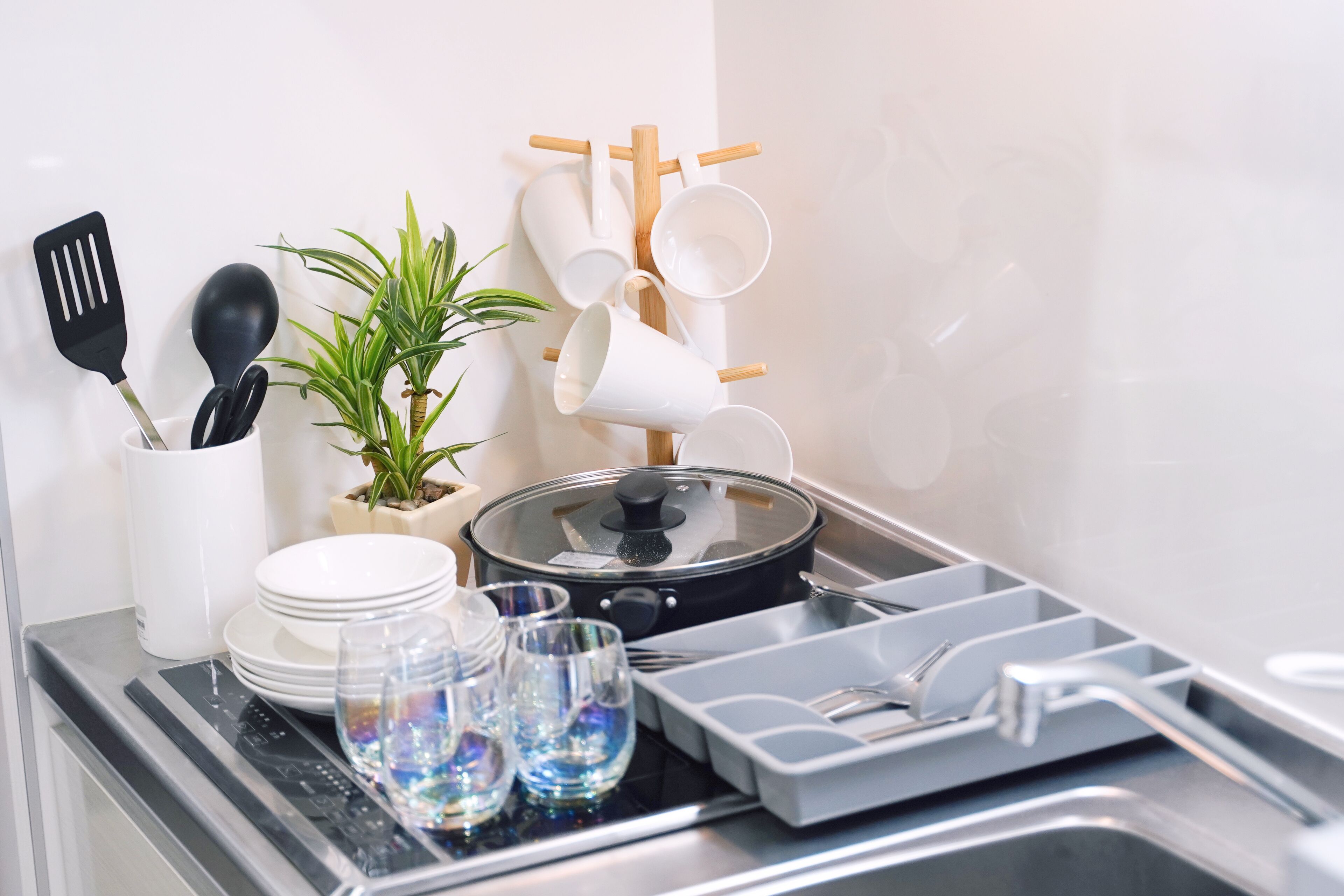 A kitchen counter with a stove, a pot, a plant, and various kitchen utensils.