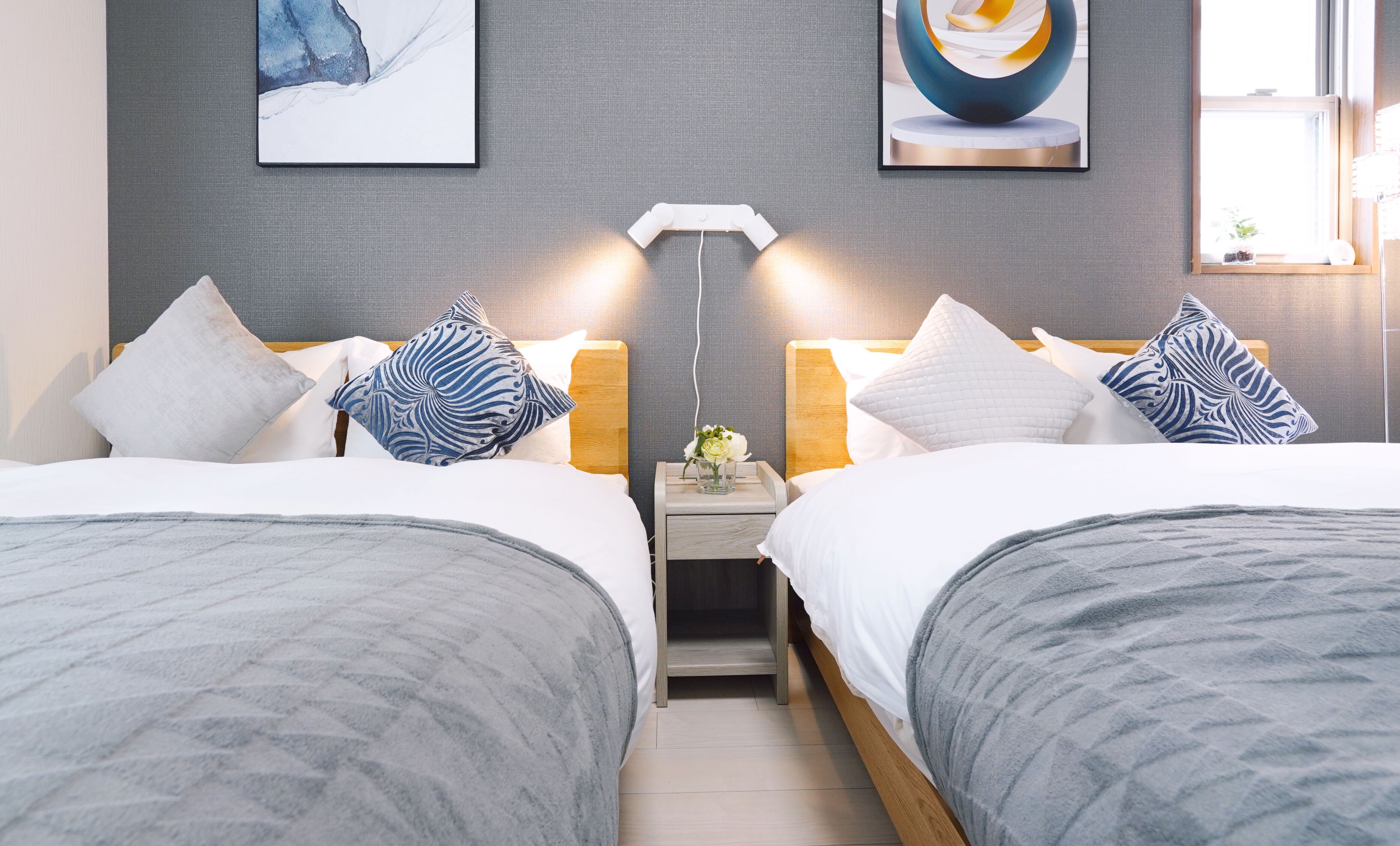 A double bed room with grey bedding, a bedside table with a vase of flowers, and two wall-mounted lamps.