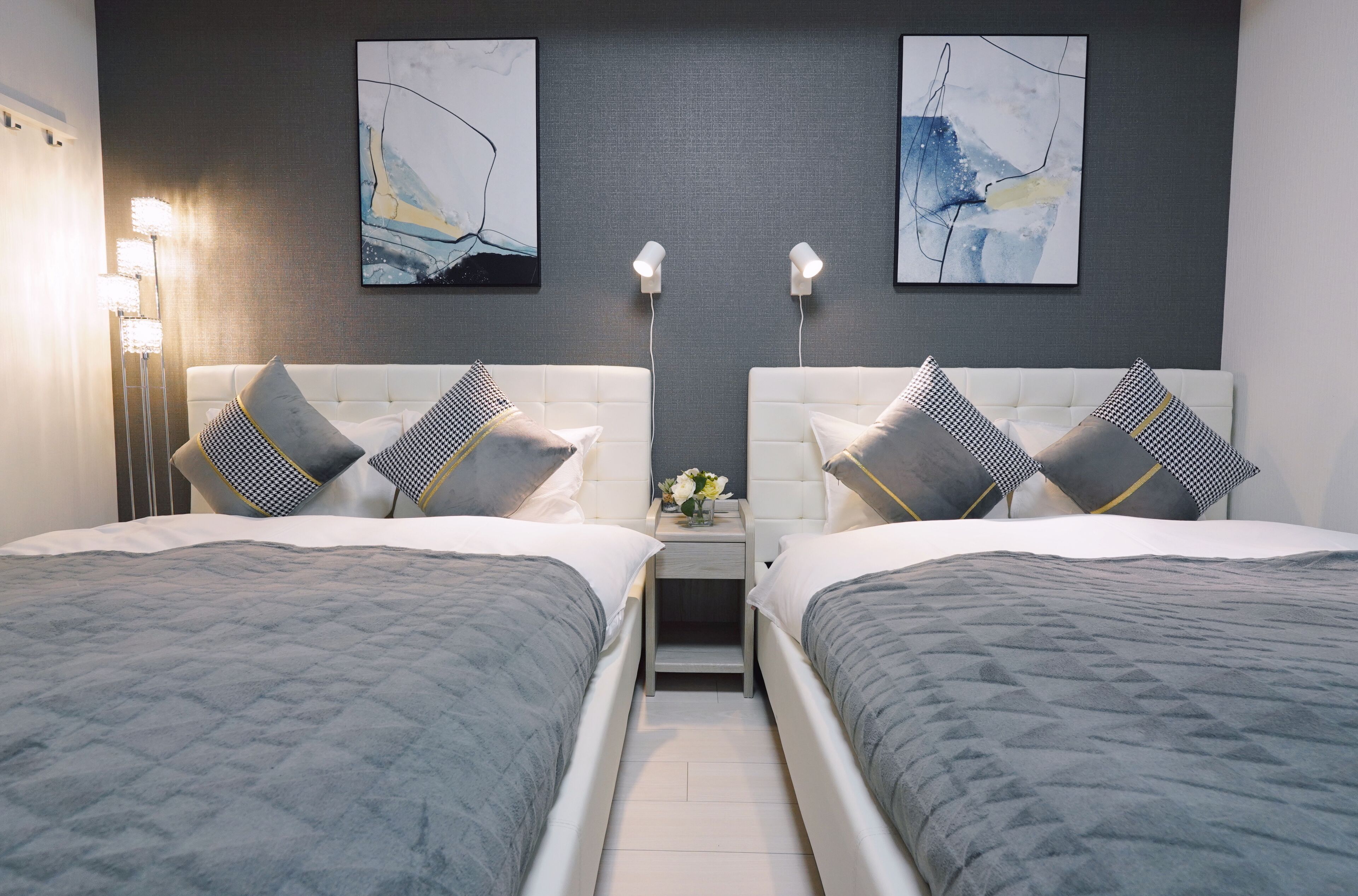 A hotel room with two beds, a nightstand with a vase of flowers, and abstract art on the walls.