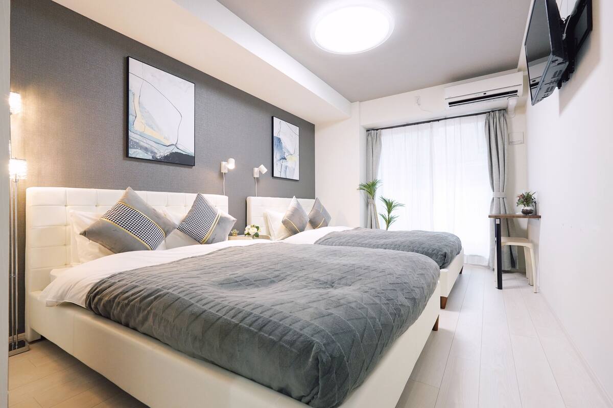 A modern hotel room with two beds, a flat-screen TV mounted on the wall, and a large window with curtains.