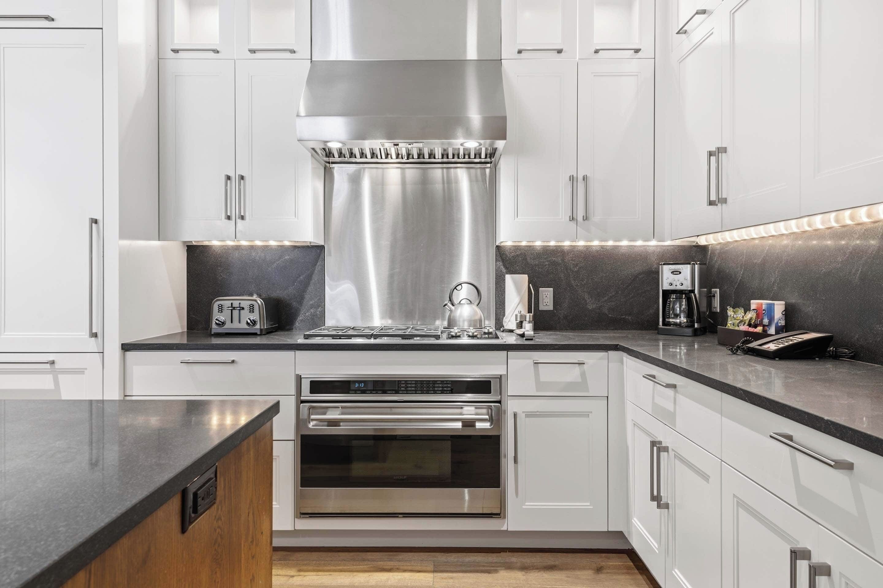 A modern kitchen with white cabinets, stainless steel appliances, and a black countertop.
