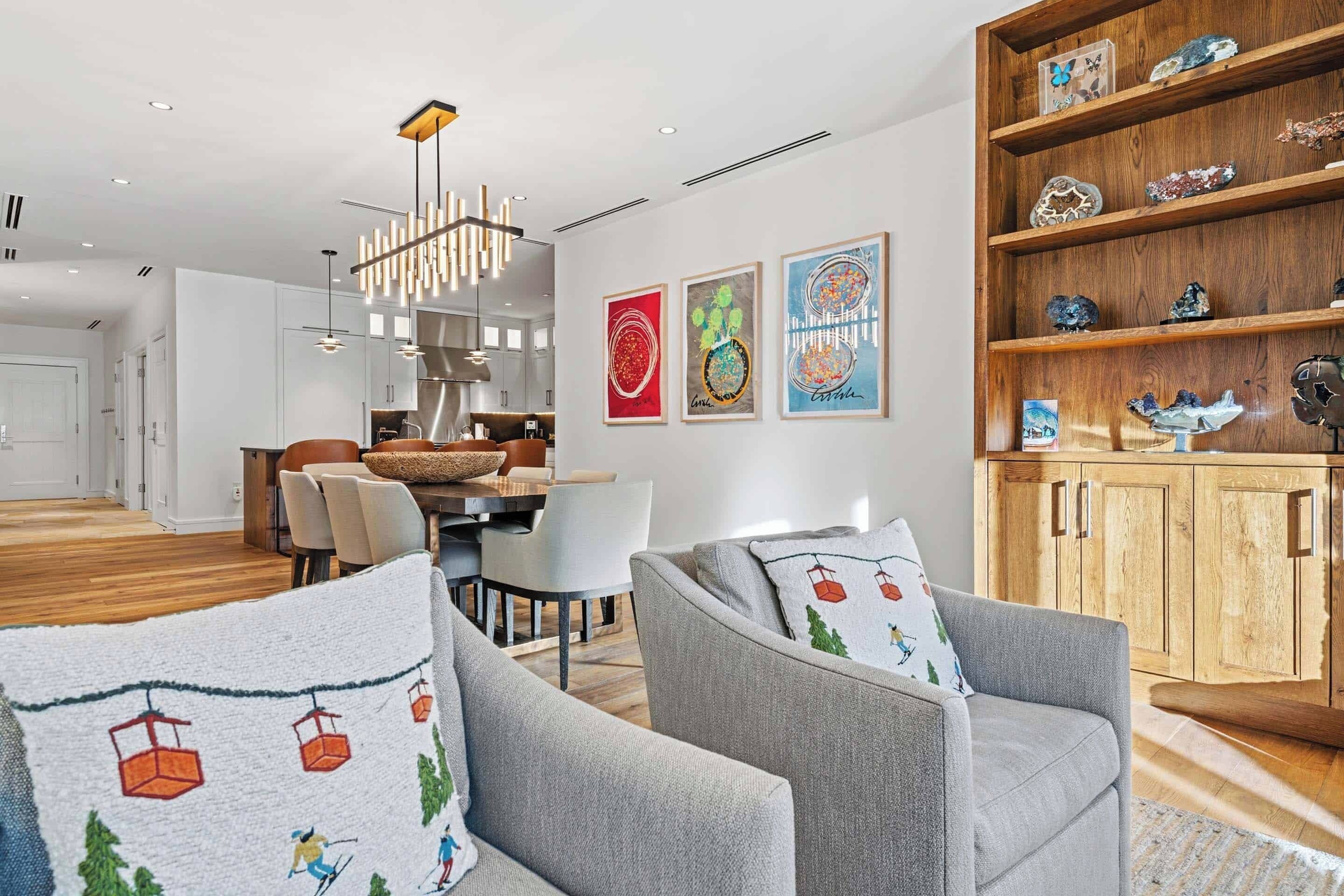 Un salon moderne avec des canapés gris, une bibliothèque en bois et un coin repas comprenant une table et des chaises.