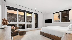 A modern bedroom with a large bed, a desk, and a view of a snowy landscape through large windows. - Solaris 6D East - 4 Bedroom + Den (Vail)
