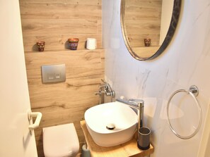 A compact bathroom with a white sink, a toilet, a mirror, and a wooden wall.