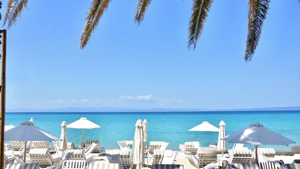 A beachside view with lounge chairs and umbrellas, a clear blue sky, and the ocean in the background. - Stay at Beachfront Villa Lilia in Pefkohori, Halkidiki for a Dreamy Vacation (Kassandra)