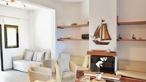 A modern living room with a sofa, armchairs, a coffee table, and a fireplace. There are wooden shelves with decorative items and a framed picture on the wall. - Stay at Beachfront Villa Lilia in Pefkohori, Halkidiki for a Dreamy Vacation (Kassandra)