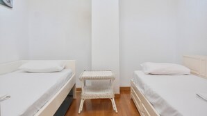 A room with two beds, a small white wicker side table, and a white wall. - Stay at Beachfront Villa Lilia in Pefkohori, Halkidiki for a Dreamy Vacation (Kassandra)