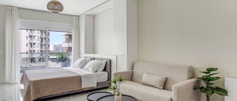Un dormitorio moderno con una cama, un sofá, una mesita y dos macetas.