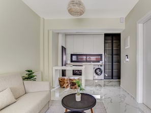 A modern living room with a sofa, a coffee table, and a kitchen area with a washing machine and a microwave.