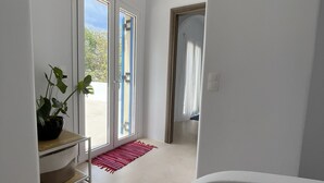 Un pasillo con pared blanca, una planta en maceta, un tapete rojo y una puerta que da a un espacio exterior.
