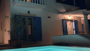 Un edificio de dos pisos con piscina delantera, balcón y puerta con contraventanas.