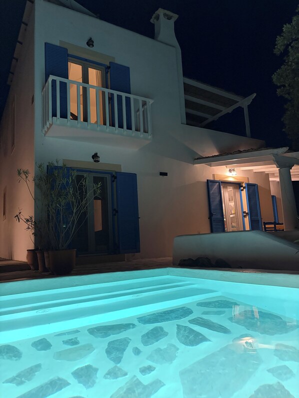 A two-story building with a swimming pool in front, a balcony, and a door with shutters.