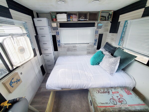 A compact, well-organized room with a bed, storage drawers, a small table, and a window with blinds. - 34ft Mobile Home Near Yale U (New Haven)